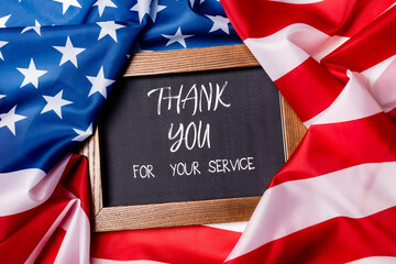 Top view of thank you for your service lettering on chalkboard on american flag
