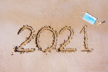 Handwriting words 2021 and medical mask on the beach