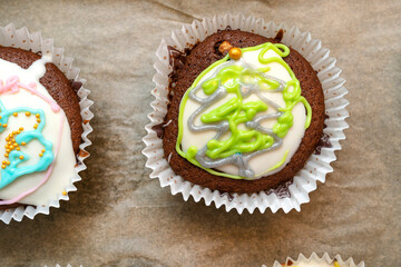 Chocolate brown muffins wrapped in white paper and covered with white frosting with colorful decorations, baked in the oven, lying on baking paper, top view.