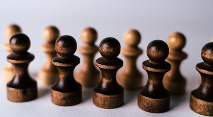 Close up of rows of black and white wooden chess pieces on white background. Selective focus on...