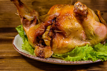 Plate with roasted whole chicken and lettuce leaves on a wooden table