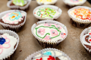 Chocolate brown muffins wrapped in white paper and covered with white frosting with colorful decorations, baked in the oven, lying on baking paper.