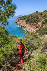 A young sports mom with a large backpack and a baby in a sling travels along the Carian trail along the sea in Turkey