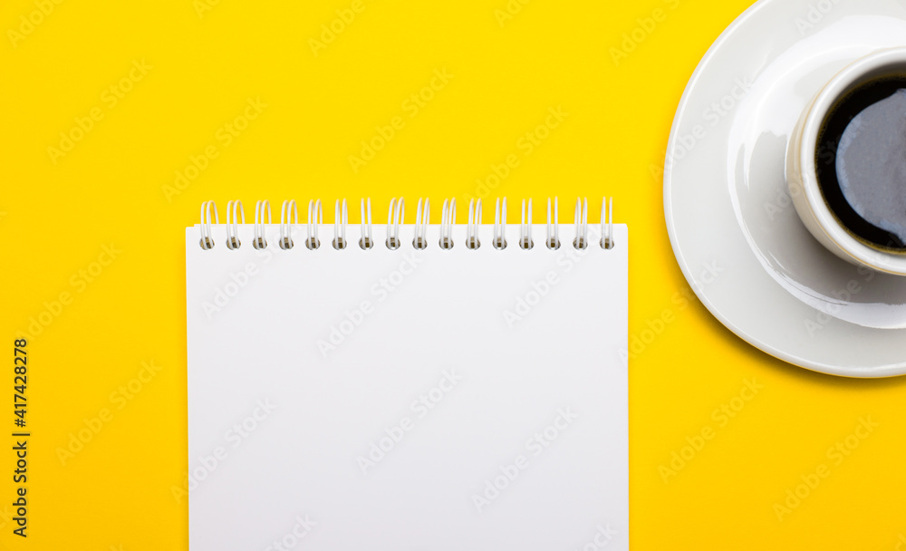 Poster on a bright yellow background, a white cup with coffee and a blank white notebook with a place to in