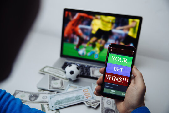 Man watching football match online broadcast on his laptop and holds smartphone with online gambling application.