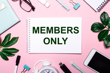 MEMBERS ONLY is written in a white notebook on a pink background surrounded by business accessories...