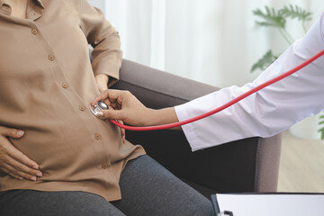 Young pregnant woman being examined by doctor, using stethoscope to check her belly and want to check the growth of the unborn child.