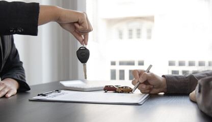 Obraz na płótnie Canvas Female attendant handed over the rental car key to the customer who signed the contract and the terms of the agreement on the document, Car rental service concept.