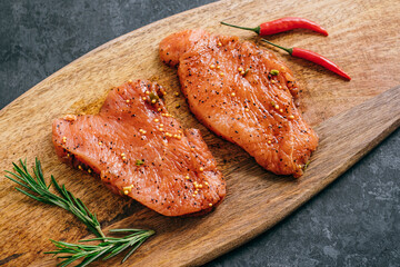 Marinated turkey steak on a wooden board with rosemary and chili pepper.