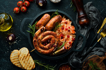 Sauerkraut and grilled sausages with rosemary and cranberries on a black plate. Traditional German dish. Top view. On a black stone background.