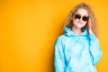 Fototapeta premium Charming woman with curly hair stands in glasses on an orange background. Summer concept