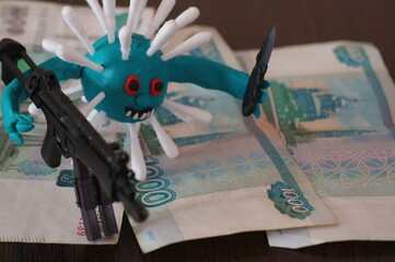 Virus figurine made of plasticine with toy weapons. Next to it are paper banknotes.