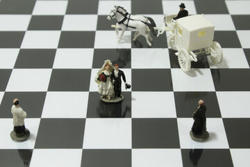 Wedding scene with the bridal couple, priest and carriage on a chessboard