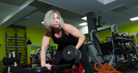 Fototapeta na wymiar A woman over fifty trains with dumbbells in the gym.