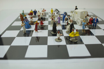 Formal dressed miniature toy pieces around a bride and a groom piece on a chessboard