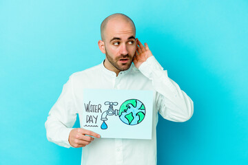 Young caucasian bald man celebrating world water day isolated on blue background trying to...