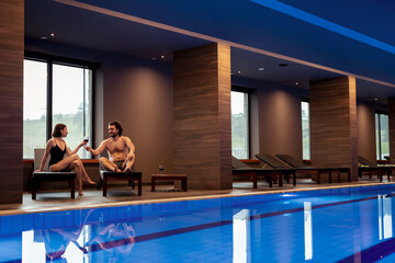 Couple drinking wine by the hotel spa center swimming pool while on vacation