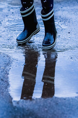 Close up child girl running and walking in puddles on rainy weather. Vertical image.