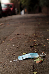 Single use face mask thrown on the asphalt sidewalk with blurred background.