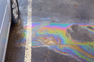 Colorful gas stain on wet asphalt. Oil stain caused by a leak under a car
