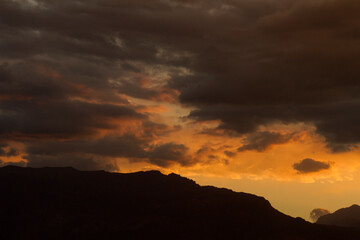Inspirational background. Dramatic sunset in the mountains. Cloudscape. View of the hills dark silhouette, beautiful clouds and sky with dusk colors.