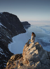 Lake Baikal in Winter. Woman Sitting on a Cliff and Looking on a Frozen Baikal lake. Olkhon Island, Russia, Siberia.