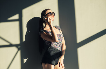 Sexy girl talking on the phone near the wall. Beautiful brunette in glasses communicates with her boyfriend.
