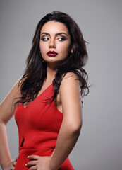 Naklejka premium Beautiful makeup woman in red dress with long black curly volume hair style, burgundy lipstick with vamp look on grey background. Closeup