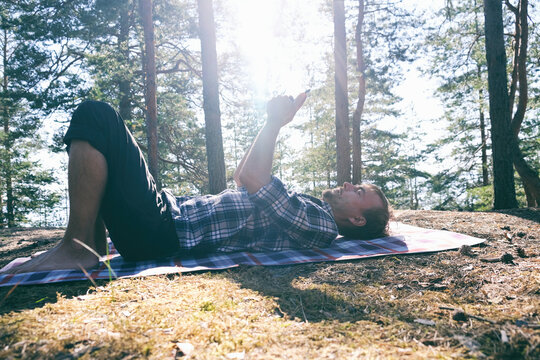 Handsome Guy Lies On Blanket In Park And Views A Feed On His Smartphone. Millennial Man Using Mobile Device Outdoor To Connect With Friends. Humanizing Tech.