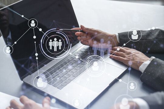 Two HR specialists analyzing the recruitment market using laptop to boost the intern program at international consulting company. Social networking hologram icons.