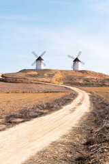 two windmills in the countryside with dirt road and straw blue sky, donquijote fields in castilla la mancha in spain europe
