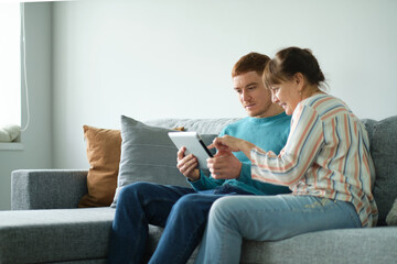 son teaching his mother to use tablet. older people using technology. Cheerful elderly woman sitting on the sofa next to his adult son