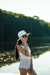 Sexy girl talking on the phone in the park.Gorgeous slender brunette talking on the phone by the lake.Smiling woman talking outdoors.