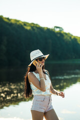 Sexy girl talking on the phone in the park.Gorgeous slender brunette talking on the phone by the lake.Smiling woman talking outdoors.