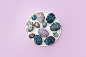 Easter eggs of blue, lilac, purple in a white plate on a colored background. Easter. Layout top view