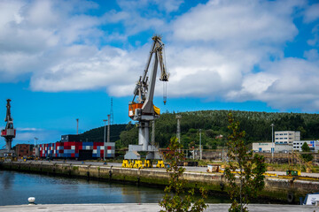 Fototapeta na wymiar Antigua grúa industrial junto al muelle de un puerto, con construcciones cercanas y una colina al fondo