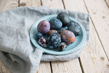 Painted Easter eggs with a marble pattern in blue, purple colors. In a blue plate on a wooden white table. Top view image.