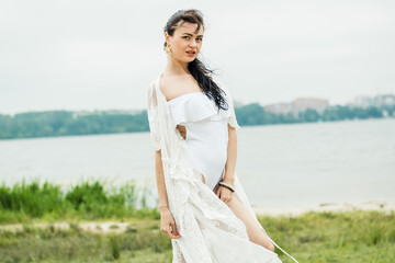 Fototapeta na wymiar Sexy girl in a white dress on a background of the lake.