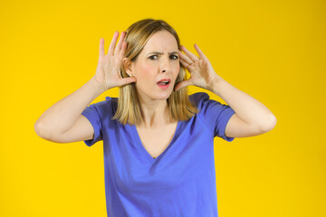 Young woman over isolated yellow background listening to something by putting hand on the ear