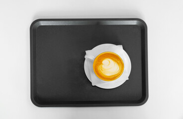 a white cup of cappuccino coffee with a saucer on a black tray on a white table. Drawing of a heart on coffee. Top view.