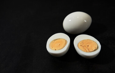 Minimalistic restaurant menu. Whole boiled chicken egg, peeled from shell, lies on table, and next to it cut egg so that yolk is visible.