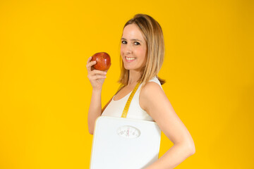 Beautiful woman holding an apple with scales over yellow background
