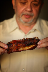The man is eating fried pork ribs. Man bites meat. Unhealthy food.