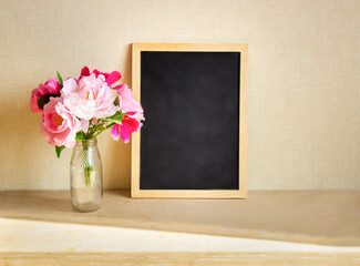 a vase of flowers stands on a wooden table in the rays of the sun on the background of a blackboard for text
