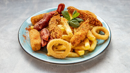 Sausage, crispy chicken, onion rings and potato chips on a blue plate