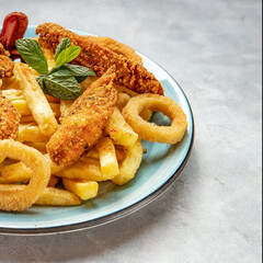 Sausage, crispy chicken, onion rings and potato chips on a blue plate