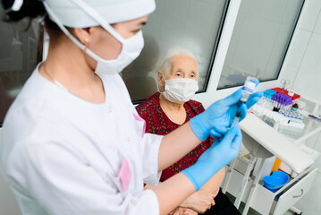 a nurse wearing a mask and rubber gloves is preparing to vaccinate an elderly woman against viral diseases. Prevention of coronavirus infection