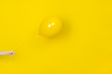 Female hand hold flying yellow balloon. Party or present concept. Yellow Balloon and hand isolated on yellow backgroun. monochrome banner with copy space.