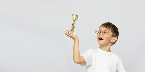 Little boy in glasses celebrates his golden trophy with copy space banner