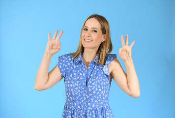 Young woman wearing casual clothes standing over blue background smiling positive doing okay sign with hand and fingers. Successful expression.